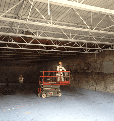 Worker operating a scissor lift inside a large warehouse with exposed beams.